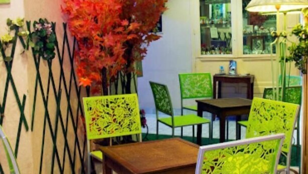 A restaurant interior with a table and chairs, a window with a view, and decorative plants. - N.D. Auxiliatrice (Lourdes)