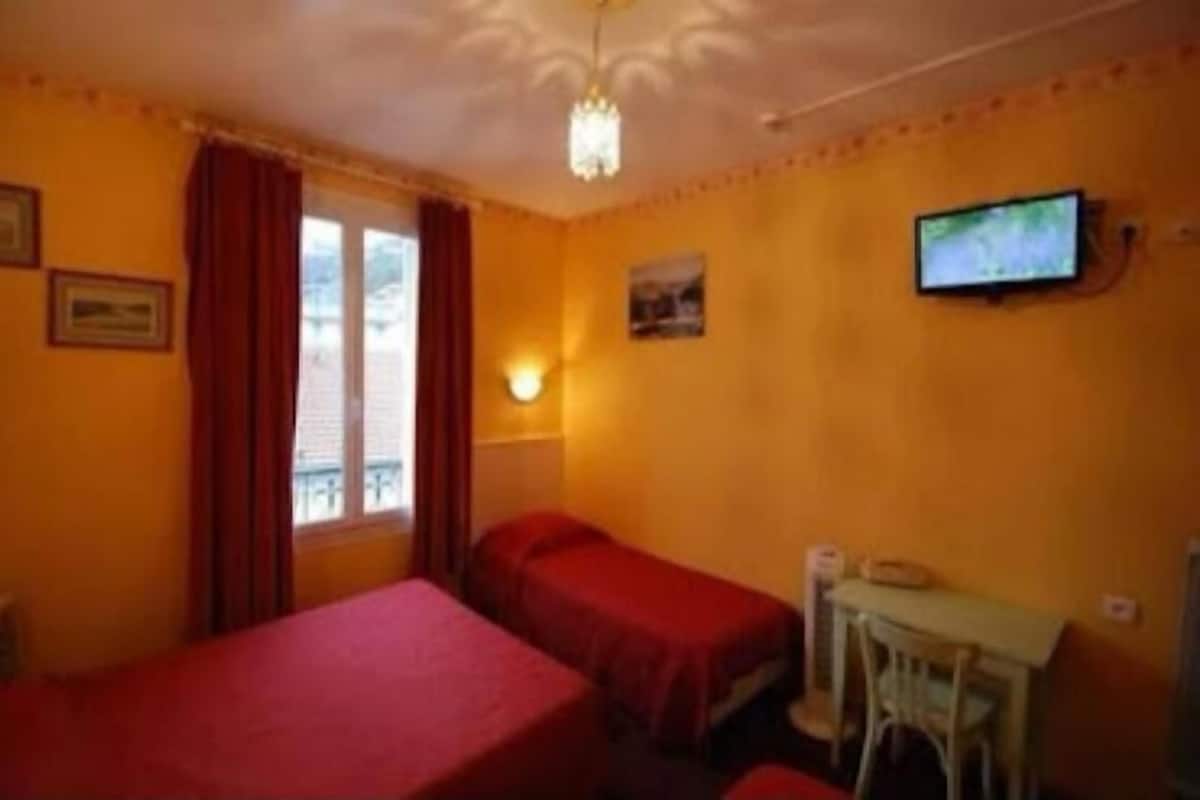 Quarto com duas camas, uma escrivaninha, televisão e janela com cortinas.