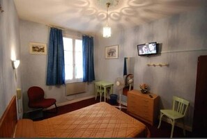 Habitación de hotel con cama, escritorio, silla, cómoda, televisor y ventana con cortinas.