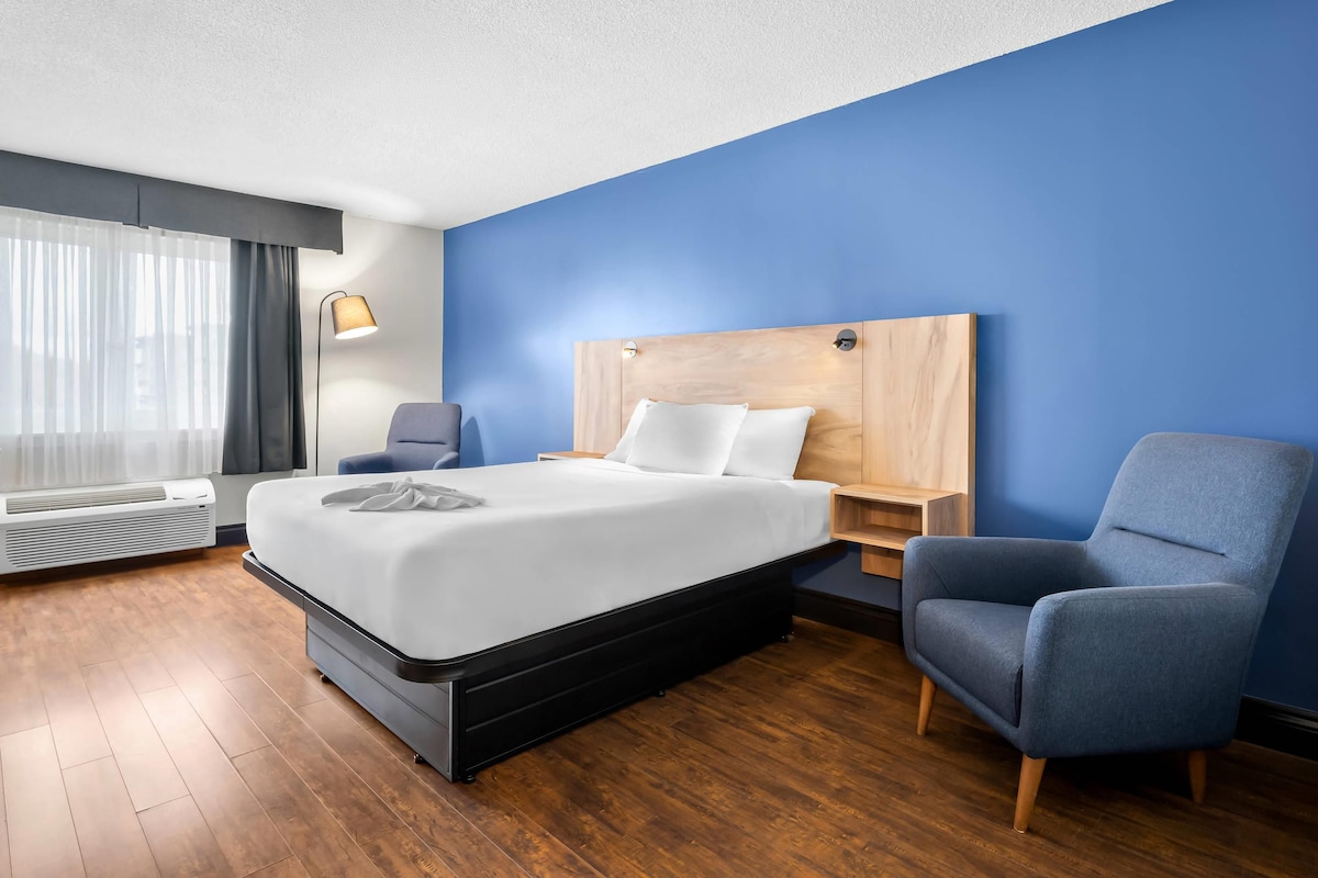 Una habitación de hotel con una cama, una silla, una mesita de noche y una lámpara.