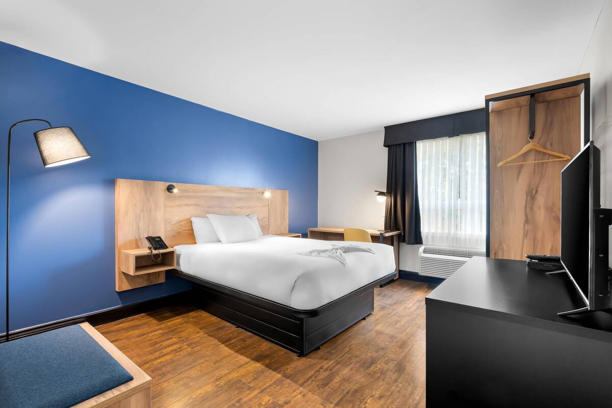A modern hotel room with a large bed, bedside tables, a desk, and a wardrobe.
