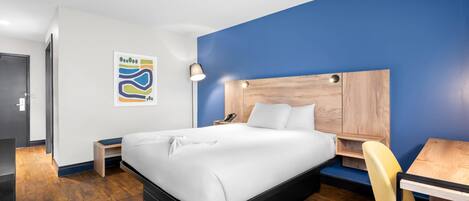 Une chambre d’hôtel moderne avec un grand lit, une tête de lit en bois, un bureau et une chaise.