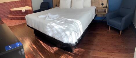 A neatly made bed with white linens and a towel, a wooden headboard, a nightstand with a lamp, and a blue armchair.