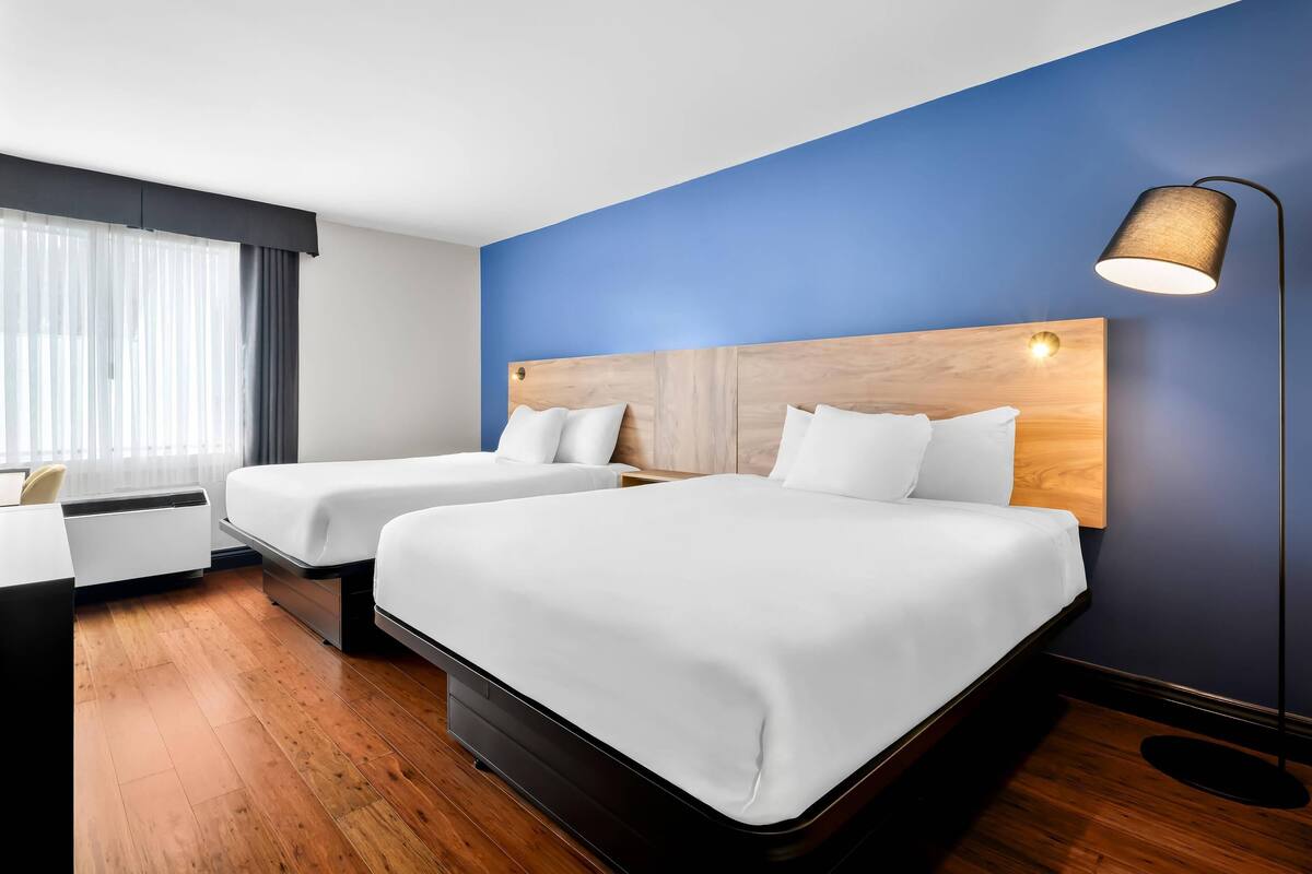 A hotel room with two beds, a desk, and a lamp.