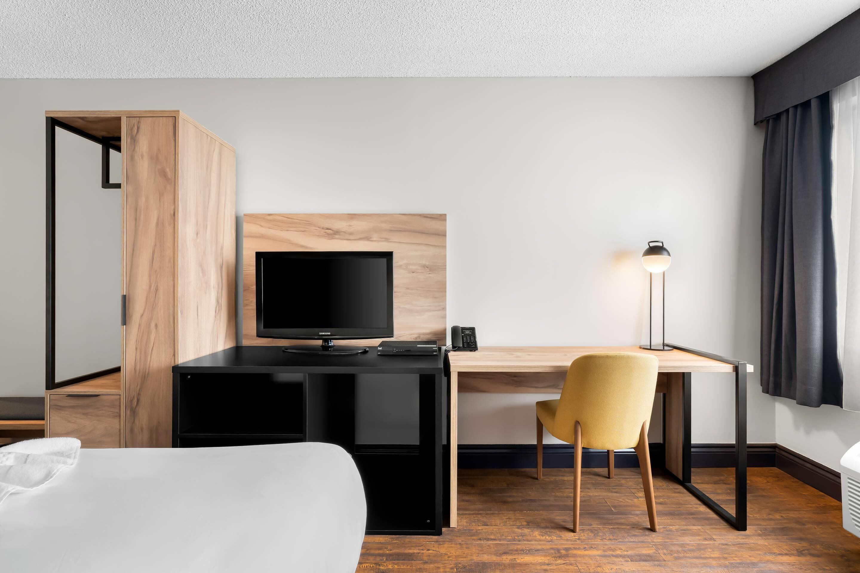 Habitación de hotel con cama, escritorio con computadora, silla, televisor y lámpara.