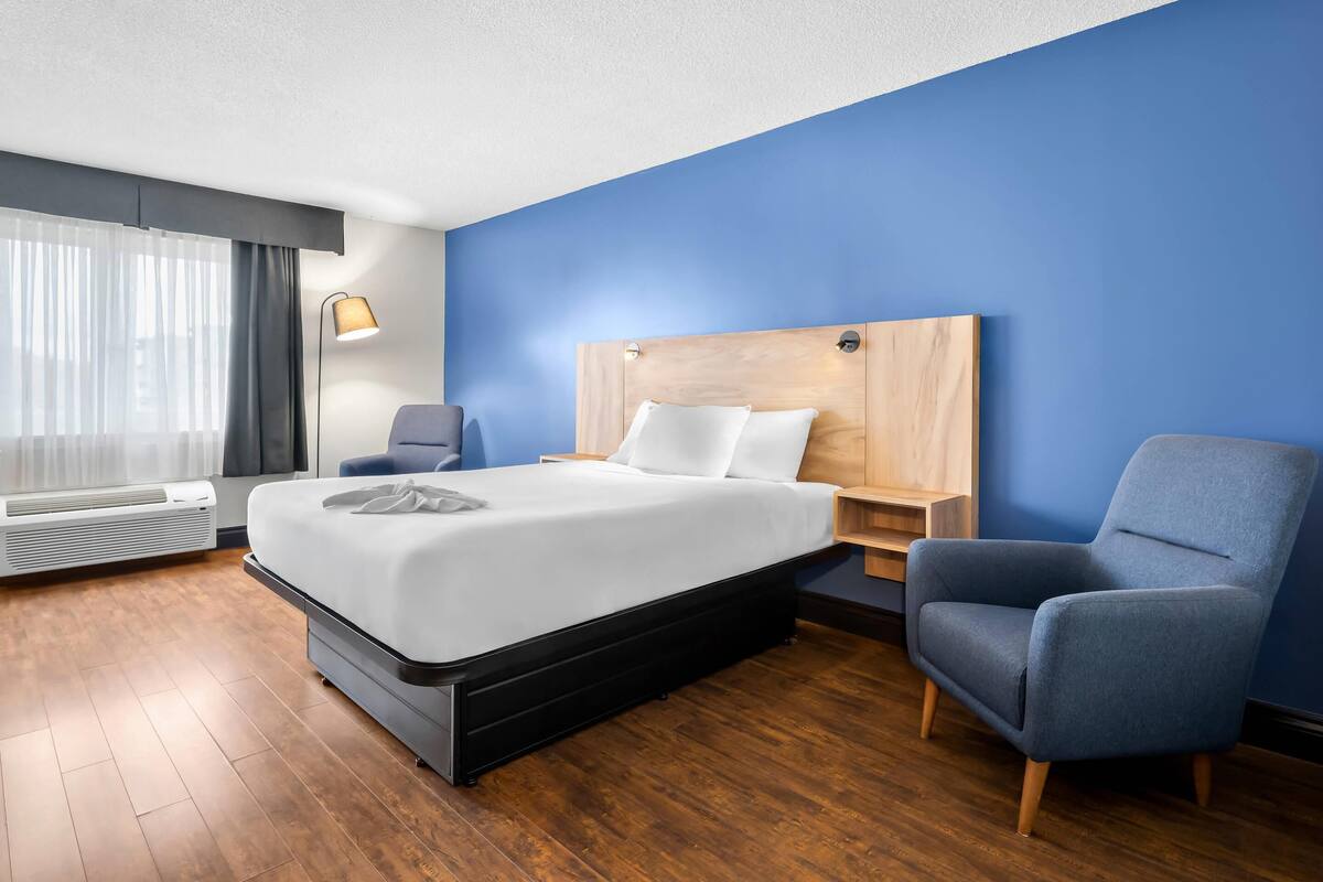 A hotel room with a bed, a chair, a nightstand, and a lamp.