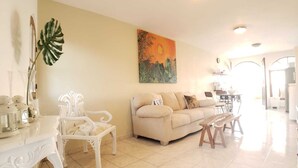 Un salon spacieux avec un canapé beige, des fauteuils blancs et un coin repas comprenant une table et des chaises.