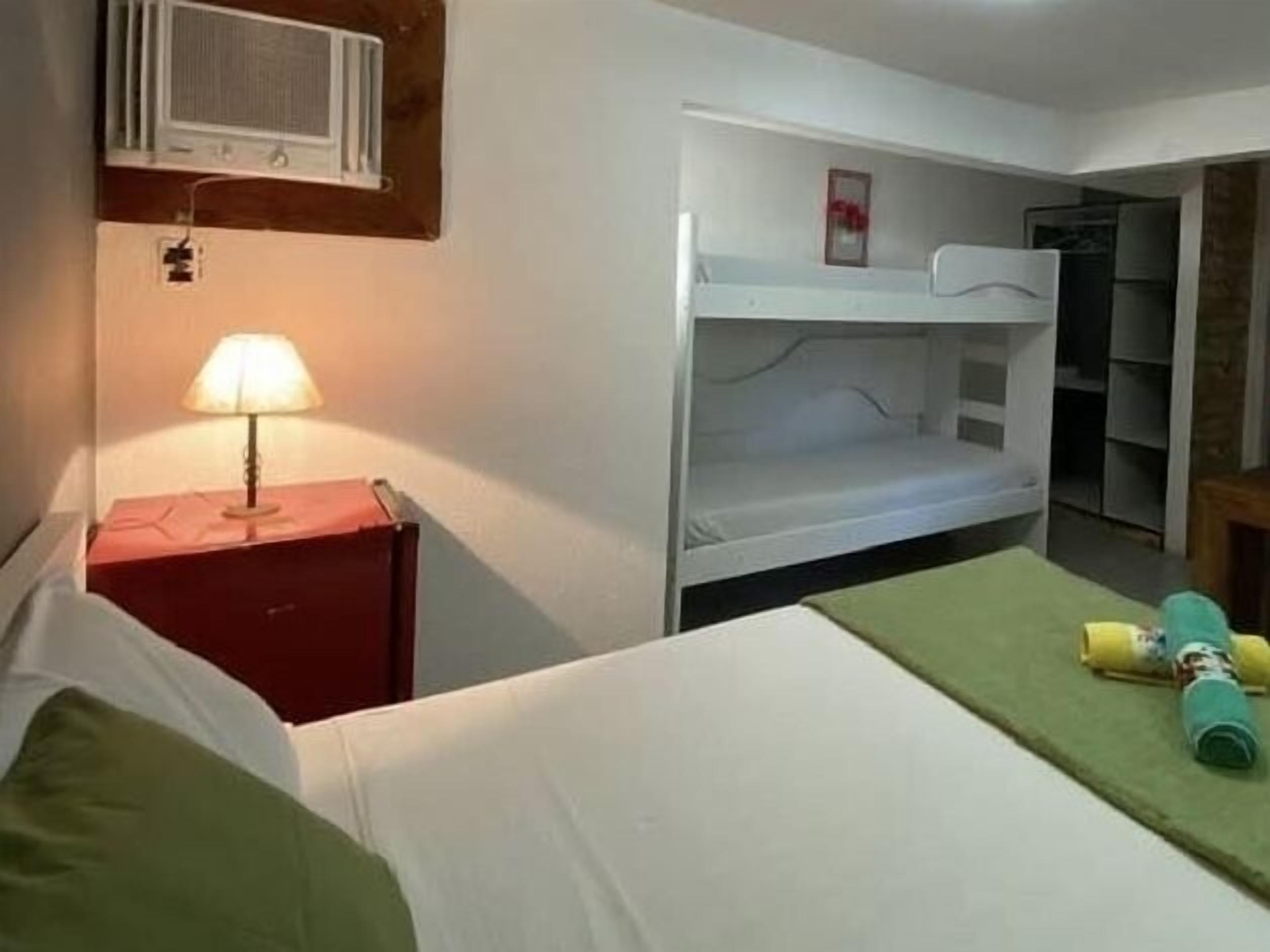 A room with bunk beds, a bedside table with a lamp, and a wardrobe.