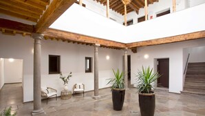 Un amplio patio con suelo de piedra, vigas de madera y columnas. Hay plantas en macetas y zonas de estar.