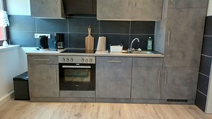 A modern kitchen with grey cabinets, a built-in oven, a coffee maker, and a sink.