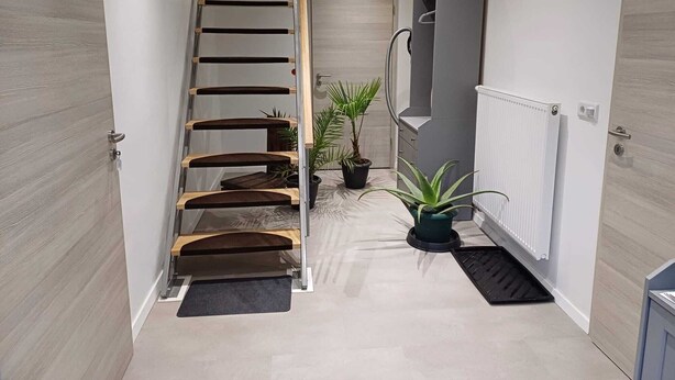 A modern interior with a wooden staircase, a radiator, and potted plants.