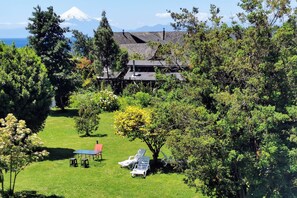Une maison avec un toit en pente, entourée d’une végétation luxuriante et offrant une vue sur une montagne enneigée.