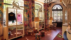 A boutique hotel interior with a vibrant, patterned curtain, a glass display case with clothing, wicker furniture, and a tiled floor. - Mama Shelter Nice (Nice)