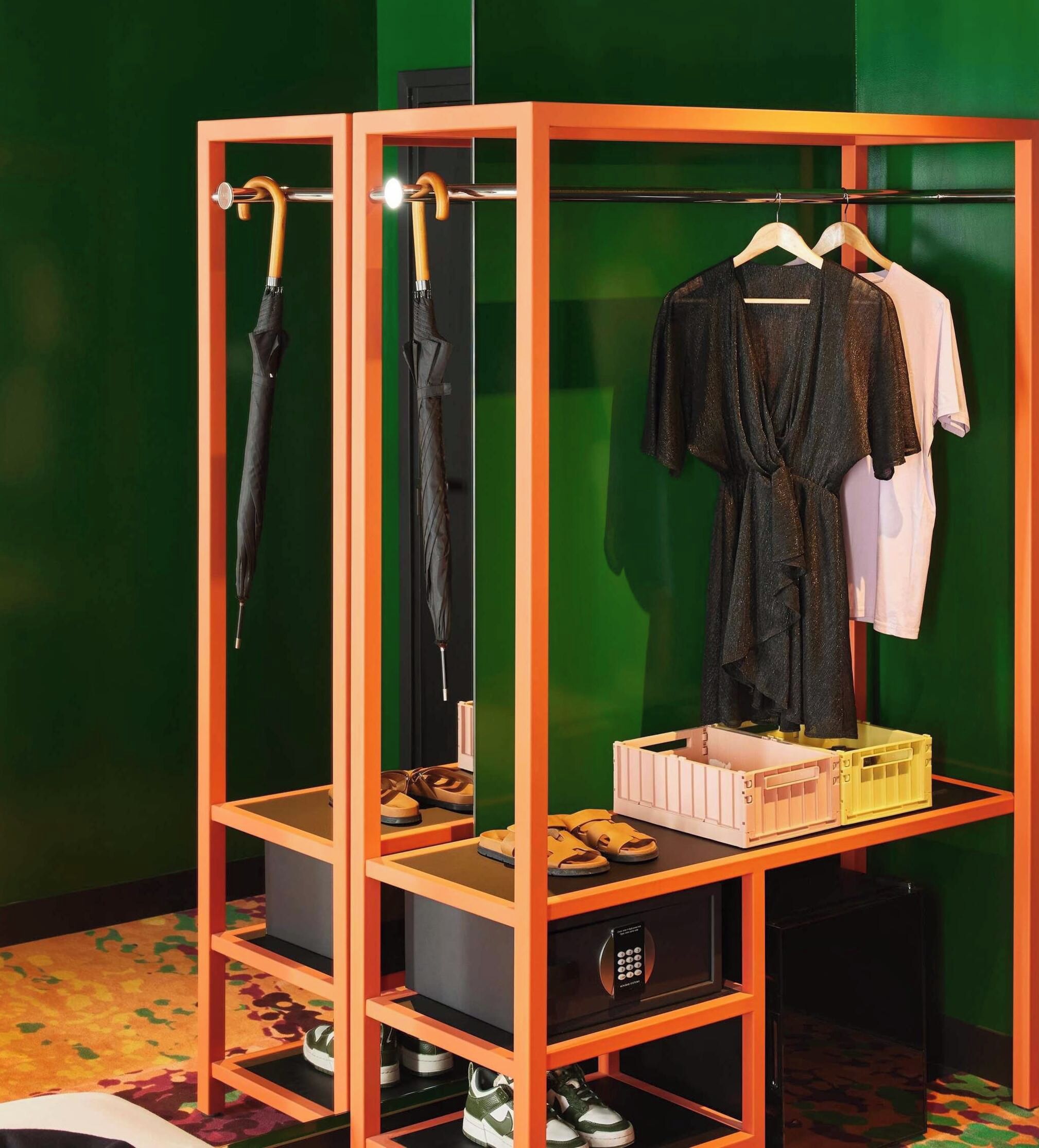 A room with a wooden wardrobe containing shoes, a black umbrella, and a hanging rack with clothes.