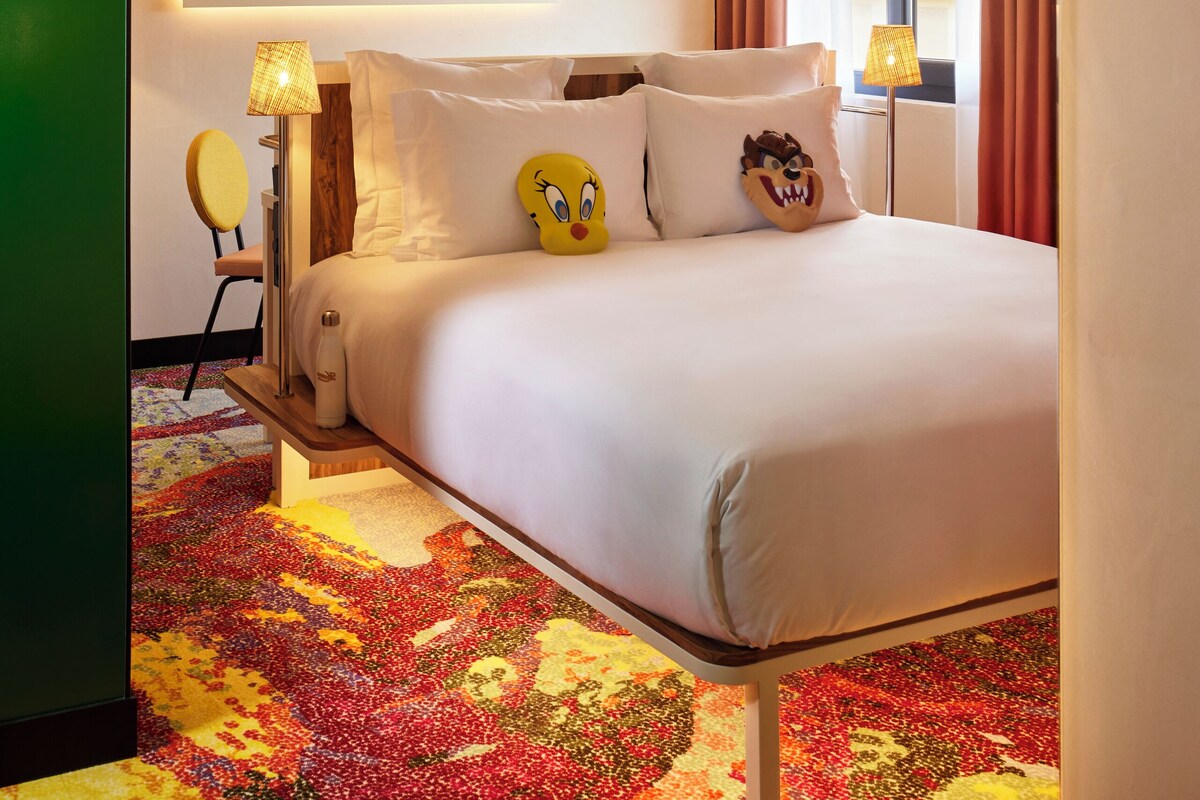 Quarto de hotel com cama, espelho, abajur e janela com cortinas.