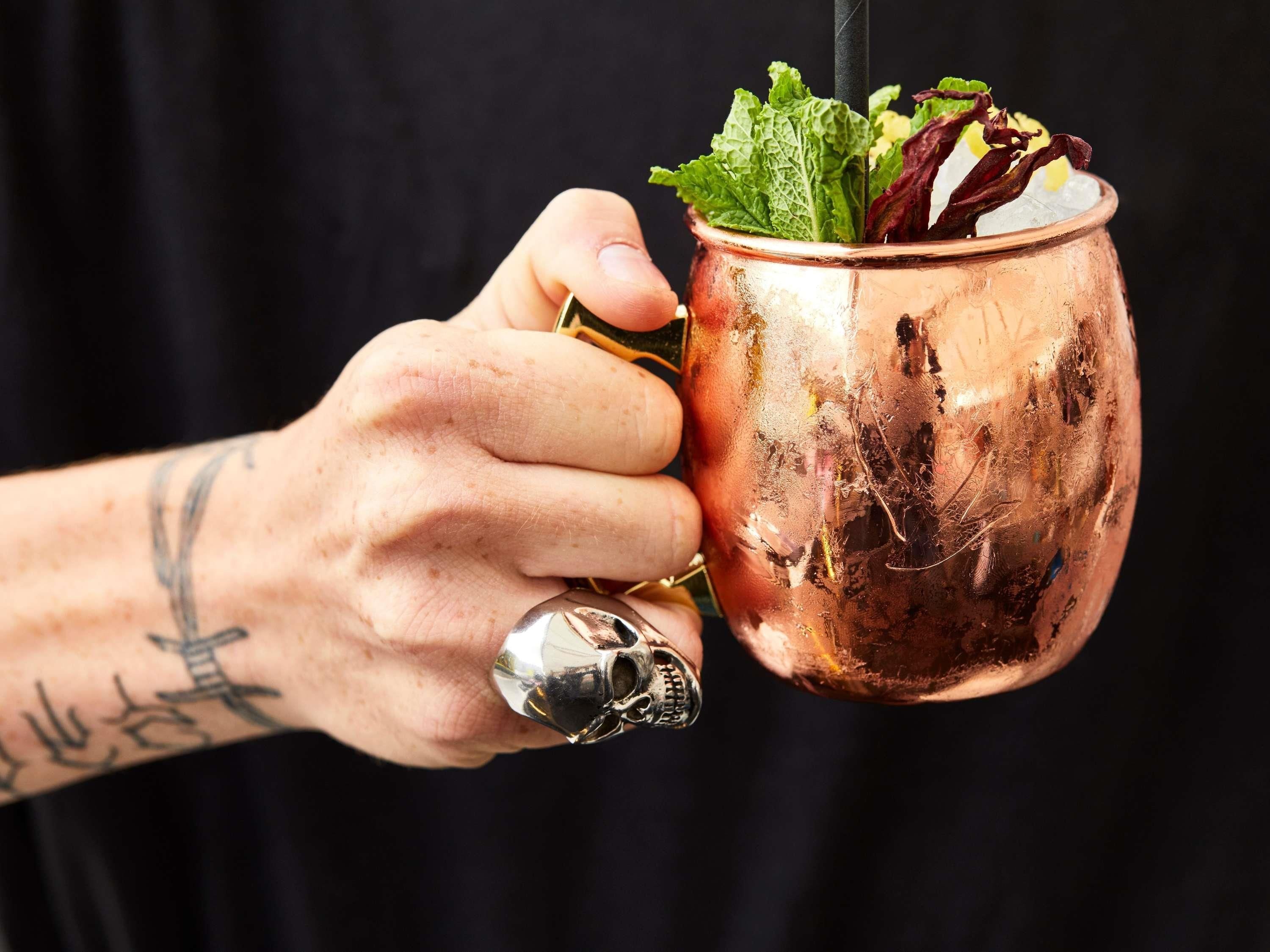 A hand holding a copper mug with a plant and ice cubes.