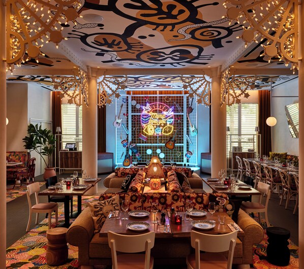 A spacious dining area with a long table set for multiple guests, surrounded by comfortable seating. - Mama Shelter Nice (Nice)
