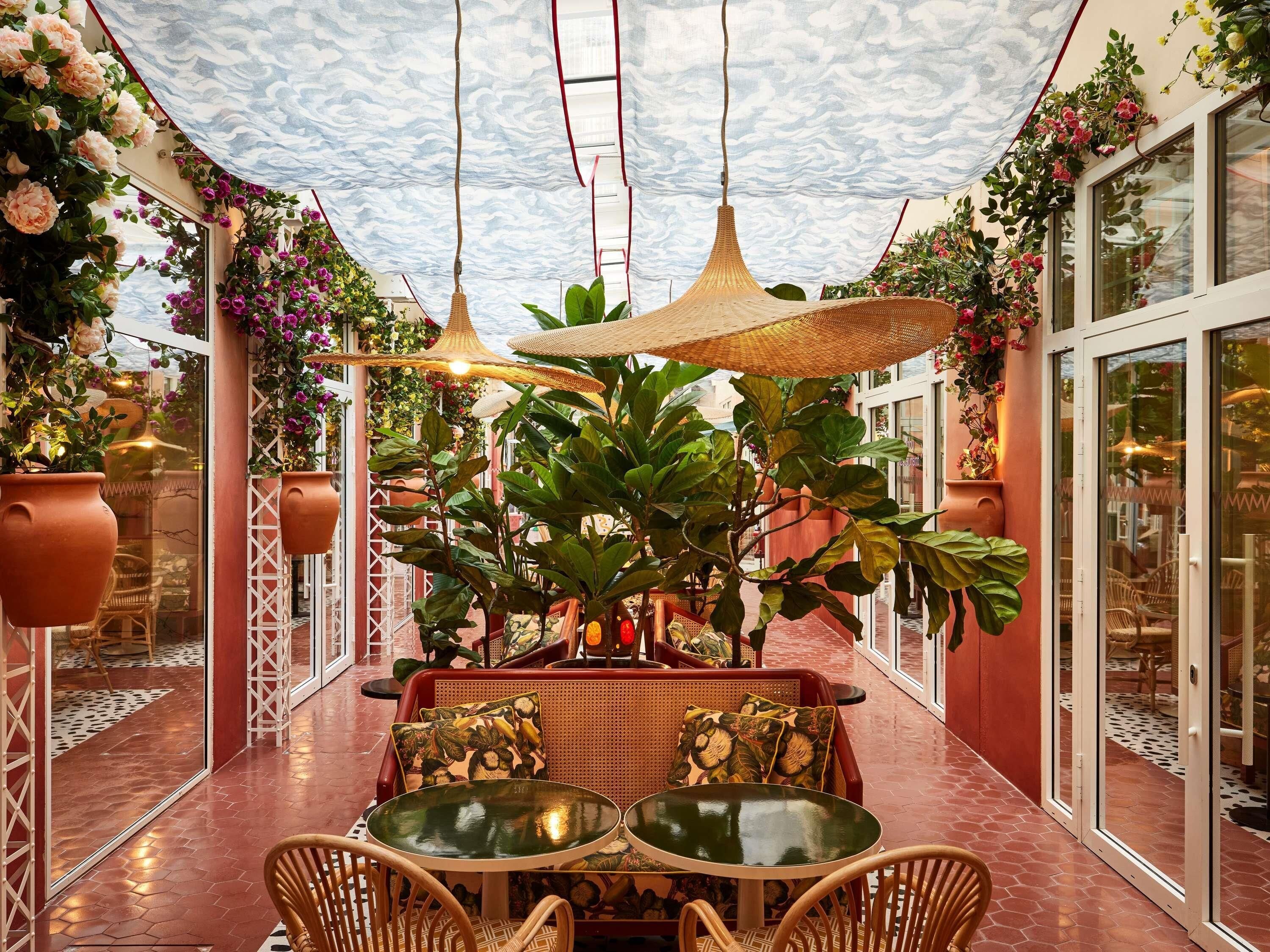 An indoor patio area with a table and chairs, surrounded by potted plants and hanging lamps.