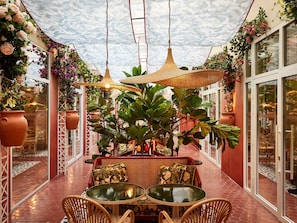 An indoor patio area with a table and chairs, surrounded by potted plants and hanging lamps. - Mama Shelter Nice (Nice)