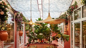 An indoor patio area with a table and chairs, surrounded by potted plants and hanging lamps. - Mama Shelter Nice (Nice)