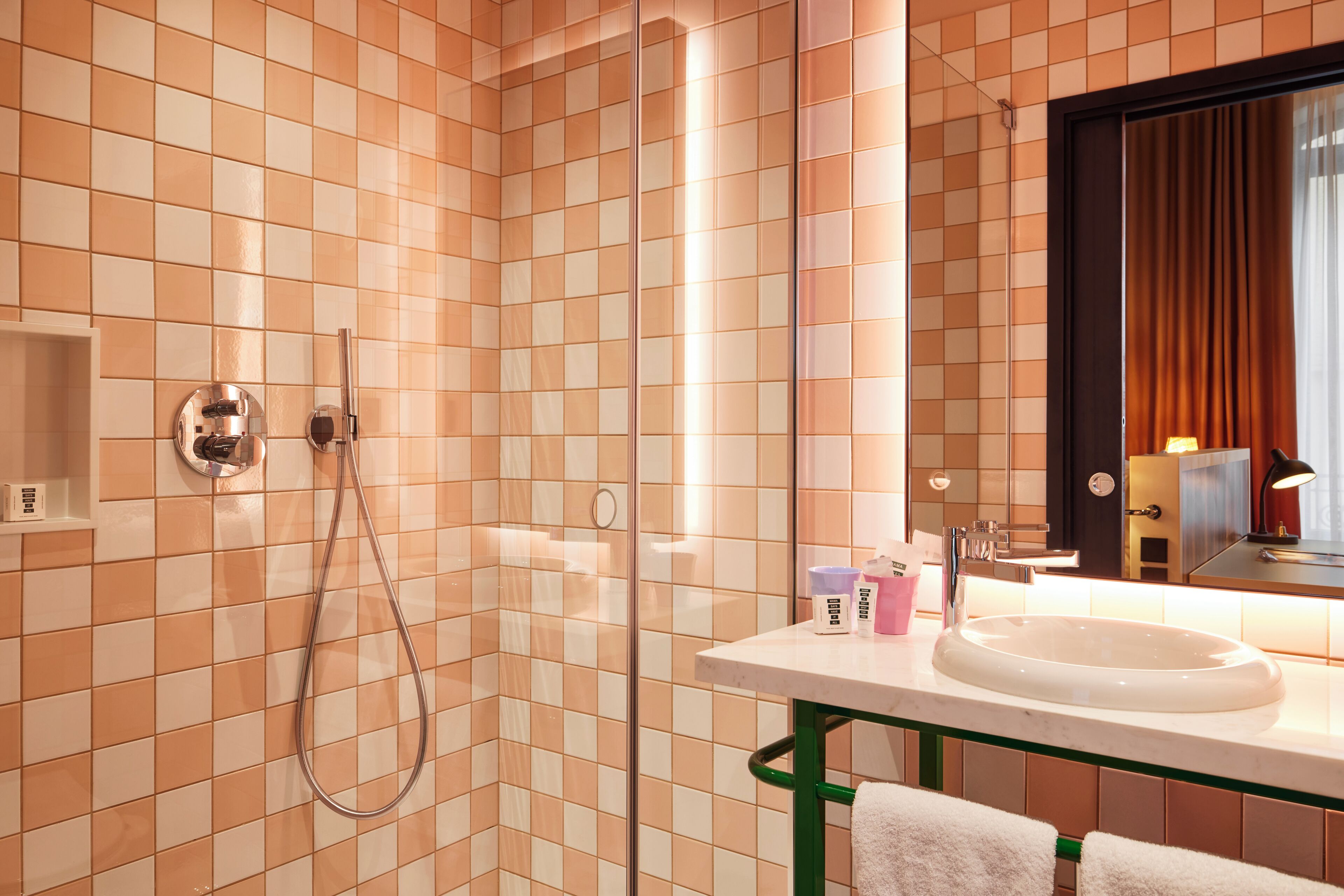 A bathroom with a tiled wall, a sink, a mirror, and a shower.