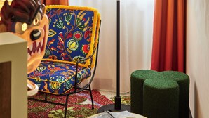 A room with a colorful chair, a lamp, a small table with a mug, and a decorative item on a desk. - Mama Shelter Nice (Nice)