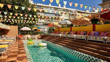 Zona de piscina con baldosas de diseño cuadriculado, sillones de descanso y sombrillas.