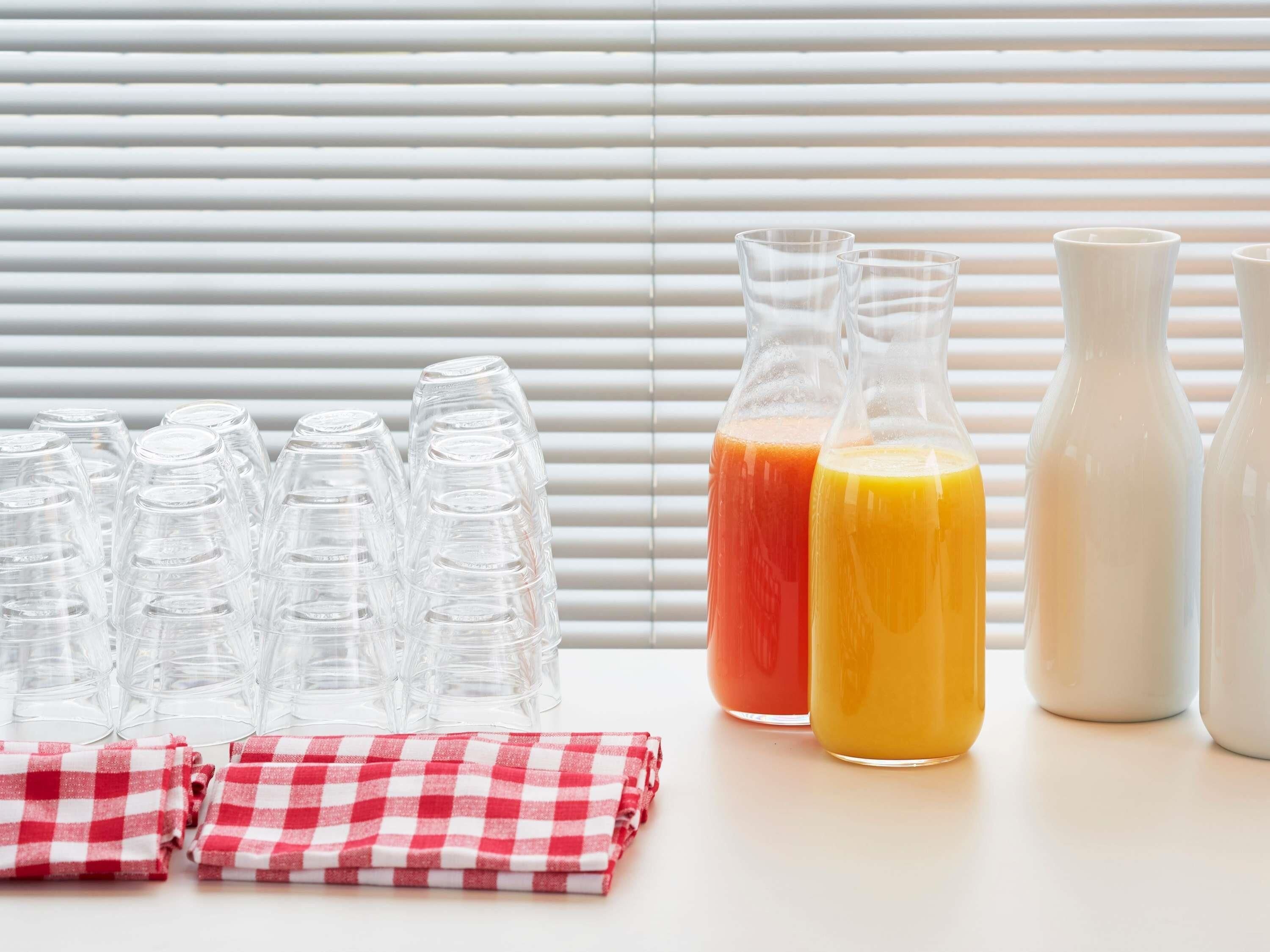 A table with stacked plastic cups, two glass bottles with orange and yellow liquids, and a red and white checkered cloth.
