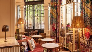 A room with a round red sofa, multiple tables, and a patterned carpet. - Mama Shelter Nice (Nice)