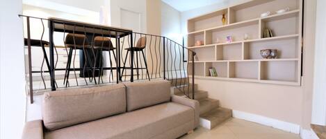 A living room with a beige sofa, a staircase, and a bookshelf.