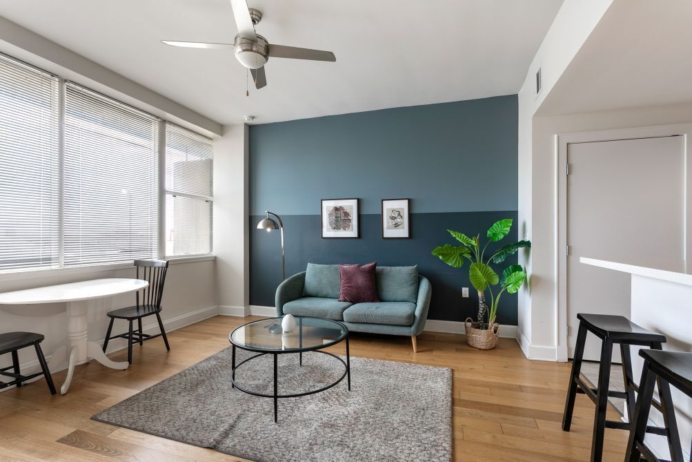 Una sala moderna con una pared de acento azul oscuro, un ventilador de techo, un sofá, una mesa de centro y una planta en maceta.