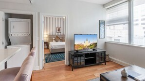 Een moderne hotelkamer met een flatscreen televisie, een bed met gestreepte gordijnen, een eethoek en een groot raam met zonwering.