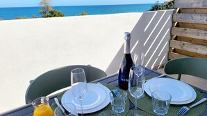 A table set for two with a bottle of champagne, glasses, and a jug of orange juice, overlooking a beach.