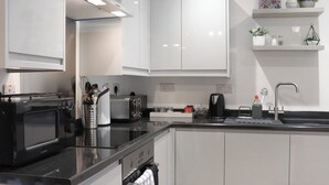 Une cuisine moderne avec des meubles blancs, un plan de travail noir, un four à micro-ondes, un grille-pain et un évier.