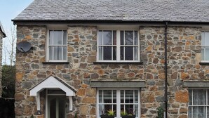 Une maison en pierre avec une entrée à pignon, de nombreuses fenêtres et un petit porche agrémenté de plantes en pot.