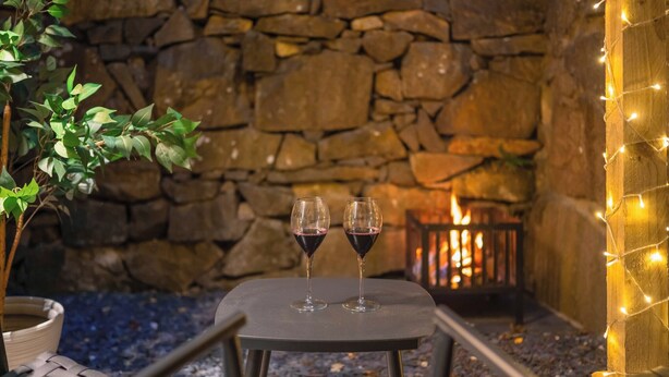 Un mur de pierres, une table avec deux verres à vin et un petit feu.
