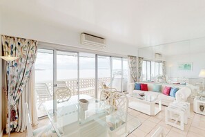 A bright living room with a glass table, white furniture, and a balcony with white chairs. - Oceana Suites Vanguardia  (Punta del Este)