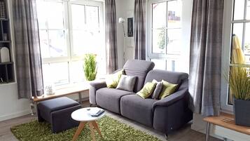 Ein Wohnzimmer mit grauem Sofa, einem kleinen runden Tisch und einem grünen Teppich.