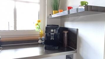 Keittiössä on kahvinkeitin, ruukkukasvi ja värikkäitä mukeja hyllyllä.