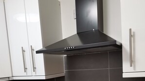 Una cocina con gabinetes blancos, una campana extractora negra y una placa de inducción negra.