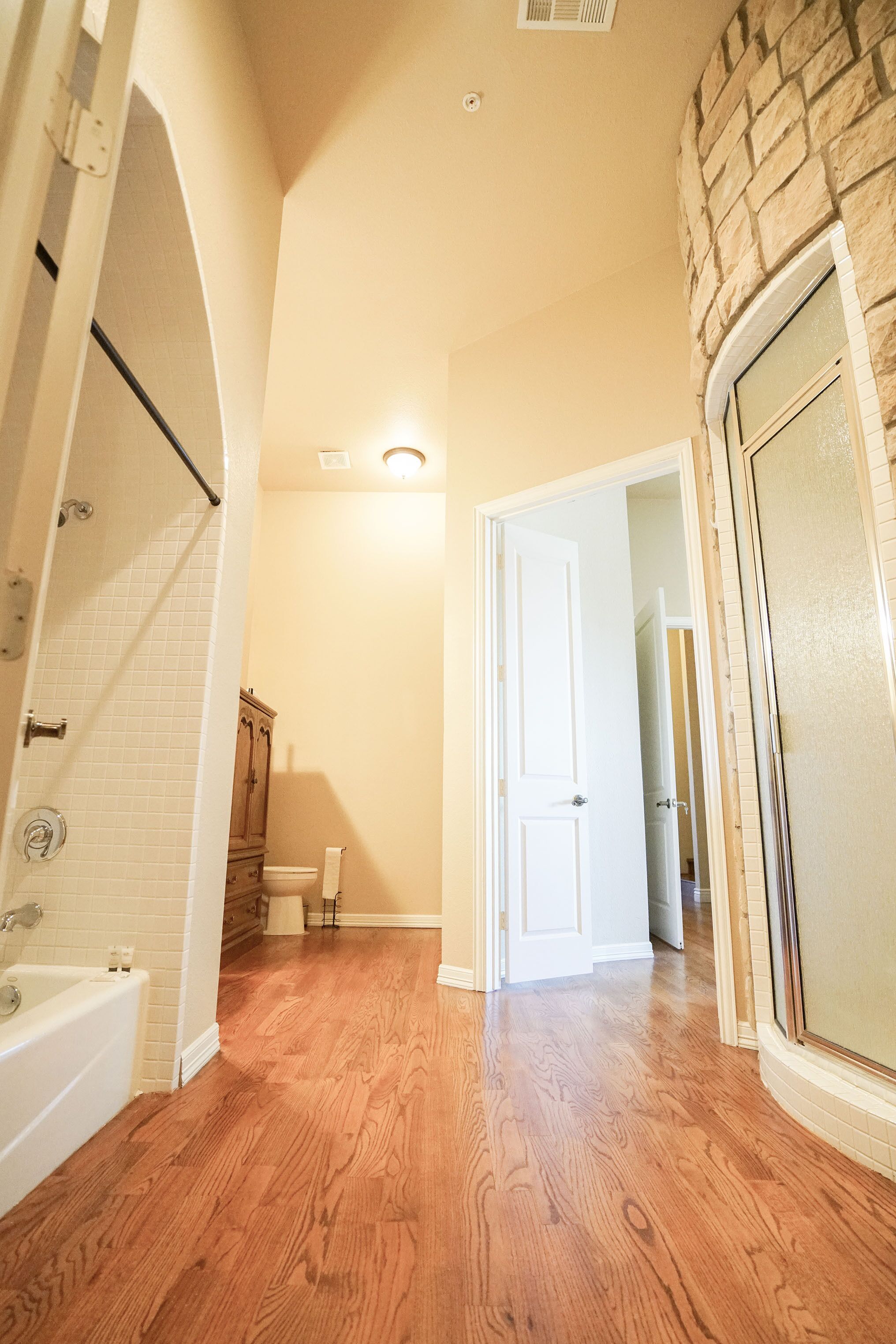 Une salle de bain spacieuse avec un plancher en bois, une baignoire blanche et un mur décoratif en pierre.