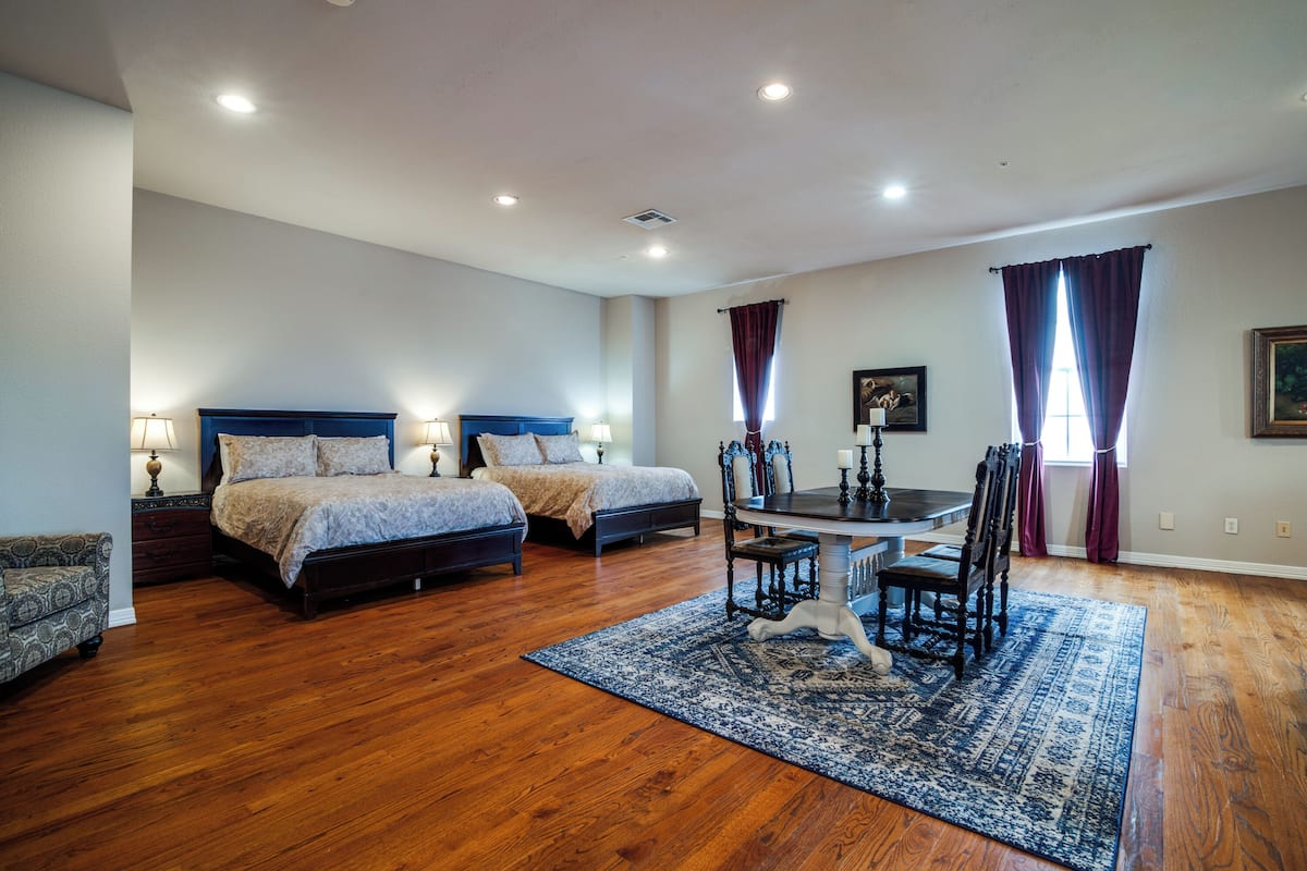 A bedroom with two beds, a dining table with chairs, and a patterned rug.