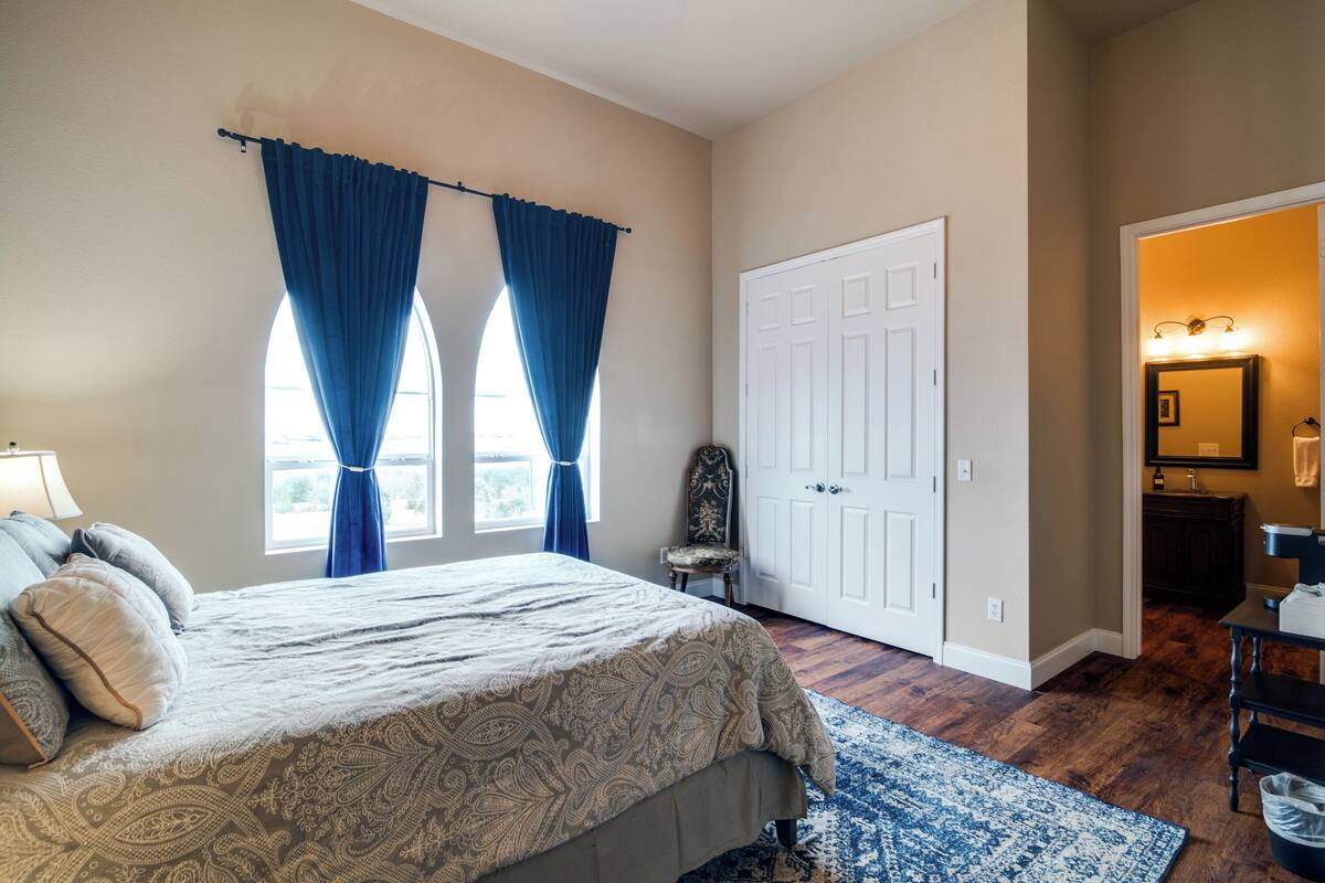 A bedroom with a bed, a chair, a door, and a bathroom visible through an open door.