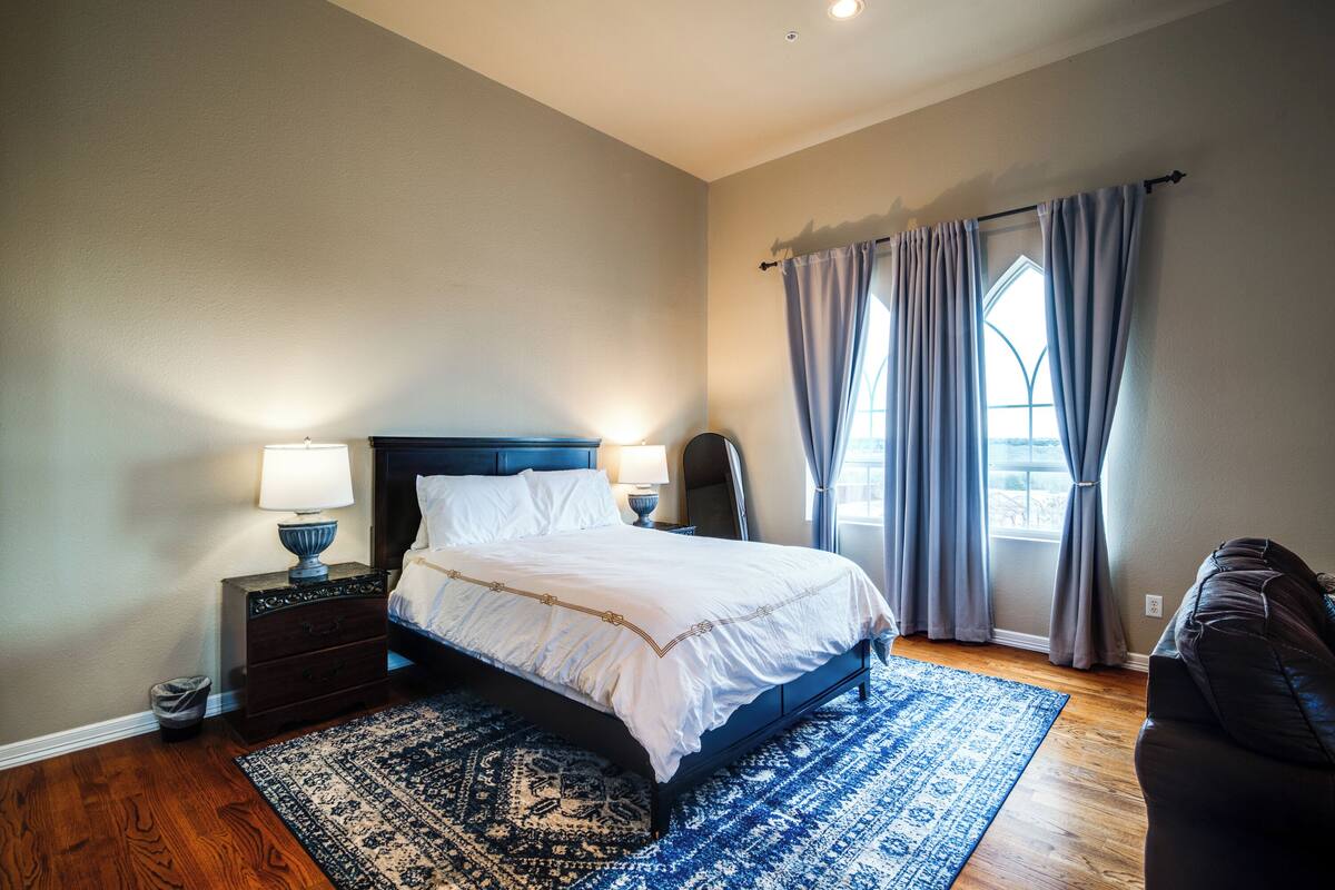 A bedroom with a bed, nightstands, a lamp, a rug, and a window with curtains.