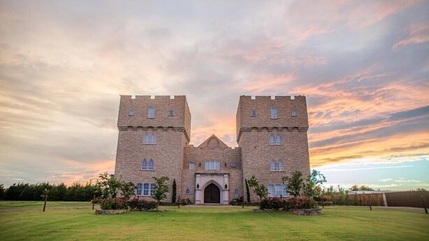 A large, castle-like building with two towers and a central entrance, surrounded by a well-maintained lawn.