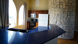 A kitchen with a stone pillar, a microwave, a refrigerator, and wooden cabinets.