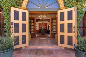 Una entrada de hotel con un patio empedrado, puertas abiertas y un candelabro.