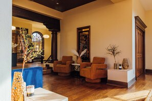Un hall d’entrée avec un plancher en bois, un canapé bleu, deux fauteuils, une table avec un vase et une porte ornée d’un panneau décoratif.