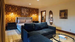 A hotel room with a bed, a sofa, a mirror, and a wall with a mosaic pattern.