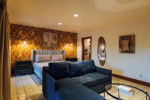 A hotel room with a bed, a sofa, a mirror, and a wall with a mosaic pattern.